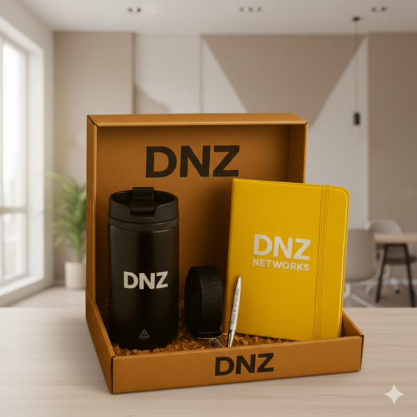 Geöffnete Onboarding‑Box aus Karton mit „DNZ“-Schriftzug, gefüllt mit schwarzem Thermobecher mit Logo, gelbem Notizbuch mit elastischem Verschluss, schwarzem Schlüsselband und silbernem Kugelschreiber – hochwertiges Willkommens‑ oder Jubiläumsgeschenk für Mitarbeitende.